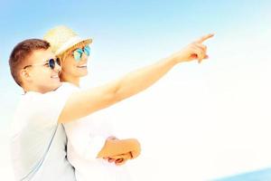 Happy couple hugging at the beach and pointing photo