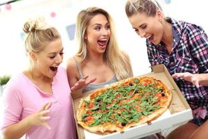Three beautiful young women eating pizza at home photo