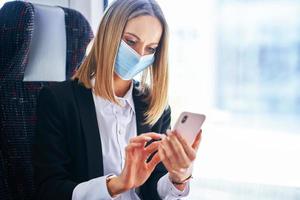 Subway commuter businesswoman in mask on public transport using smartphone