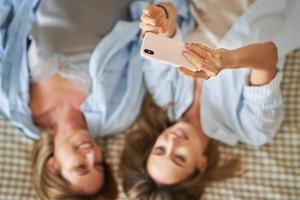 Two young girlfriends on the bed taking selfie photo