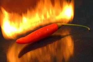 Picture of a red cayenne pepper with  fire flame and shadow below  on black background. photo