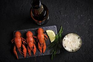 Boiled river crayfish with lemon and dill on slate and bottle with glass of foam beer.