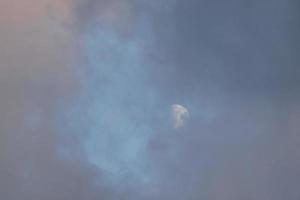 luna casi llena, vista a través de las nubes al atardecer. foto