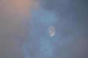 luna casi llena, vista a través de las nubes al atardecer. foto