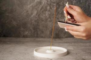 Incense stick in ceramic holder on marble table. Hand with long matches photo