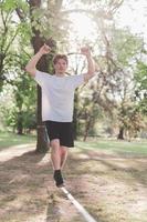 Young man balancing and jumping on slackline. Man walking, jumping and balancing on rope in park. photo