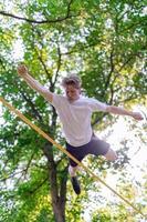 Young man balancing and jumping on slackline. Man walking, jumping and balancing on rope in park. photo