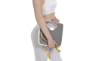 Female model holding scale and measuring tape over white background photo