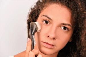 Beautiful young woman is washing her face with face brush photo