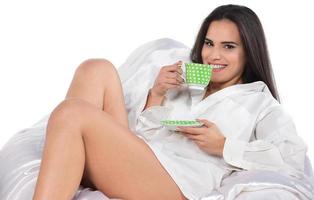 beautiful brunette woman laying in bead holding cup of coffee, tea cup photo