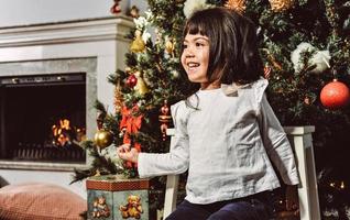 Asian little girl decorate the Christmas tree indoors. The morning before Xmas. Portrait loving girl close up. photo