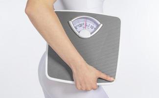 Female model holding scale and measuring tape over white background photo