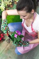 Young woman at a nursery holding flower plant in her hands as she kneels in the walkway between plants. photo