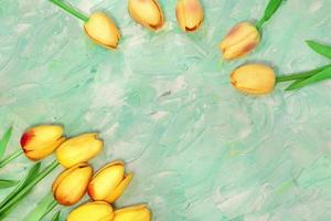 los tulipanes amarillos están dispuestos en esquina y en arco. hay lugar para texto sobre fondo verde menta con pinceladas. postal felices pascuas, 8 de marzo, día internacional de la mujer foto
