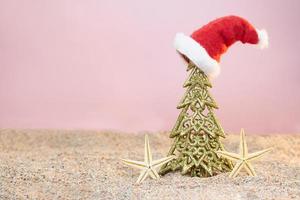 Golden Christmas tree with Santa's hat and starfish on sand. Christmas, New Year. Copy space photo
