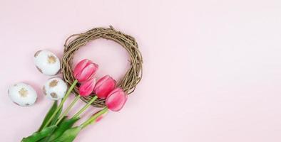 Bouquet of pink tulips with wreath, nest and white eggs with gold on pink background. Easter. Copy space photo