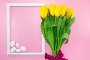 Bouquet of yellow tulips with bow with frame and white stones on pink background. Holiday, Birthday, March 8, Mother's, International Women's Day. Copy space photo