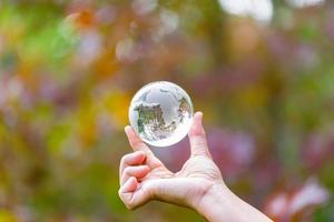 mano humana sosteniendo globo planeta cristal en bosque verde con luces de naturaleza bokeh. día Mundial del Medio Ambiente. concepto para la conservación del medio ambiente, proteger la ecología de la tierra y la vida ecológica. foto