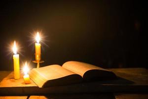 Light candle with holy bible and cross or crucifix on old wooden background in church.Candlelight and open book on vintage wood table christianity study and reading in home.Concept of christ religion photo