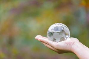 mano humana sosteniendo globo planeta cristal en bosque verde con luces de naturaleza bokeh. día Mundial del Medio Ambiente. concepto para la conservación del medio ambiente, proteger la ecología de la tierra y la vida ecológica.
