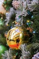 Glittery golden ball ornament hangs from bough of Christmas tree. Christmas and New Year concept. photo