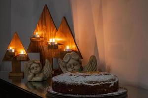 Festive Christmas setup consisting of lit candles, angel statues and a cake. photo