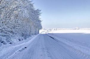 View of a snow-covered country road in winter with sunshine and blue sky.