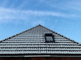 Open roof window in velux style with black roof tiles covered in snow during winter photo