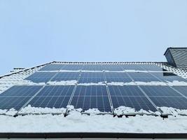 Solar panels producing clean energy on a roof covered in snow of a residential house. photo