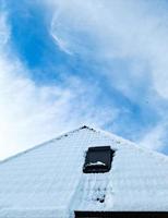 Open roof window in velux style with black roof tiles covered in snow during winter photo