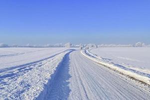 View of a snow-covered country road in winter with sunshine and blue sky. photo