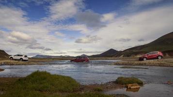 Cars driving across shallow river landscape photo