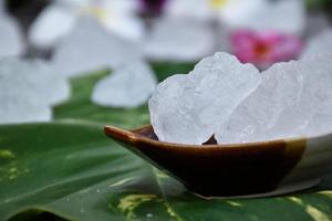 Soft focus of Alum cubes on small ceramic cup, blurred plumeria flowers background, concept for herb, bodycare, skincare, waterclear, spa, treatment, disease protection and protect armpit smell. photo