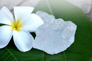 cubos de alumbre sobre maceta de cerámica y fondo de flores de plumeria, concepto de hierbas, cuidado corporal, cuidado de la piel, agua clara, spa, tratamiento, protección contra enfermedades y proteger el olor de las axilas. foto