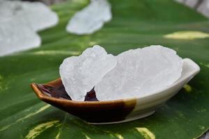 Soft focus of Alum cubes on small ceramic cup, blurred plumeria flowers background, concept for herb, bodycare, skincare, waterclear, spa, treatment, disease protection and protect armpit smell. photo