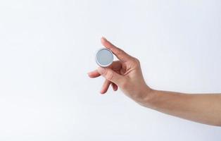 Woman hand holding blank round tin container for lip balm or cream on light gray background photo