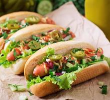 Hot dog with jalapeno peppers, tomato, cucumber and lettuce on wooden background photo