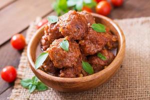 Meatballs in sweet and sour tomato sauce and basil in a wooden bowl photo