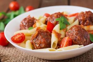 Penne pasta with meatballs in tomato sauce in a white bowl photo