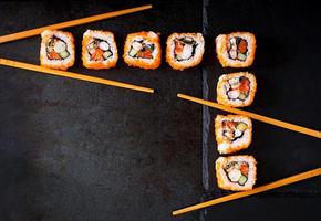 comida tradicional japonesa - sushi, rollos y palillos para sushi sobre un fondo oscuro. vista superior foto