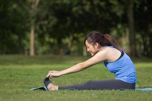 mujer asiática relajadamente practicando yoga de flexión hacia adelante o yoga de estiramiento de isquiotibiales para refrescarse después del ejercicio en el parque público foto