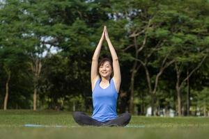 mujer asiática relajadamente practicando yoga de meditación y estirándose en el bosque para alcanzar la felicidad de la sabiduría de la paz interior para un concepto sano de la mente y el alma