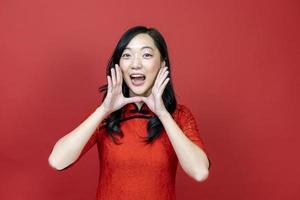 Asian chinese woman in red cheongsam or qipao calling people to wish the good luck and prosperity in Chinese New Year celebration holiday isolated on red background photo