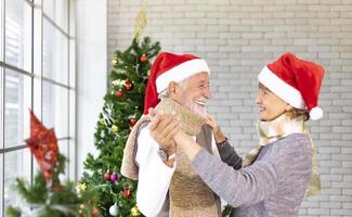 Senior Caucasian couple dancing and smiling together in happiness during Christmas holiday while wearing red Santa hat for season celebration photo