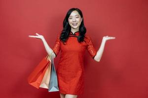 Asian chinese woman in red cheongsam or qipao holding shopping bag wish the good luck sale and prosperity in Chinese New Year celebration holiday isolated on red background photo