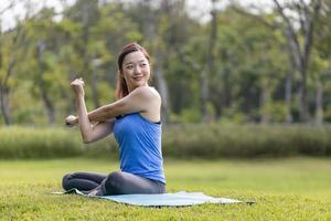 Asian woman relaxingly practicing arm and shoulder stretching yoga inside the public park for cool down after exercise in the public park photo