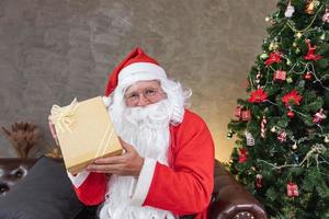 Santa Claus is holding christmas present box with fully decorated chrsitmas tree for season celebration and happy new year event photo