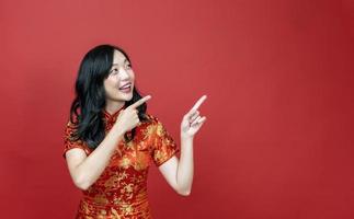 mujer asiática con cheongsam rojo o qipao apuntando al regalo para la celebración del año nuevo chino aislada en el fondo rojo foto