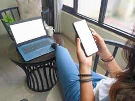 computer, blank screen phone mockup image with white background for advertising, woman's hand using laptop and mobile phone on table in cafe.mockup photo