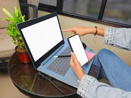 computadora, imagen de maqueta de teléfono de pantalla en blanco con fondo blanco para publicidad, mano de mujer usando computadora portátil y teléfono móvil en la mesa en cafe.mockup foto